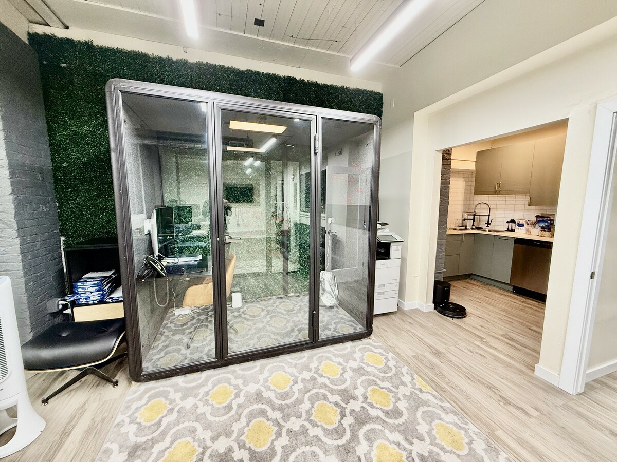 Soundproof phone pod with green wall backdrop and kitchenette beyond